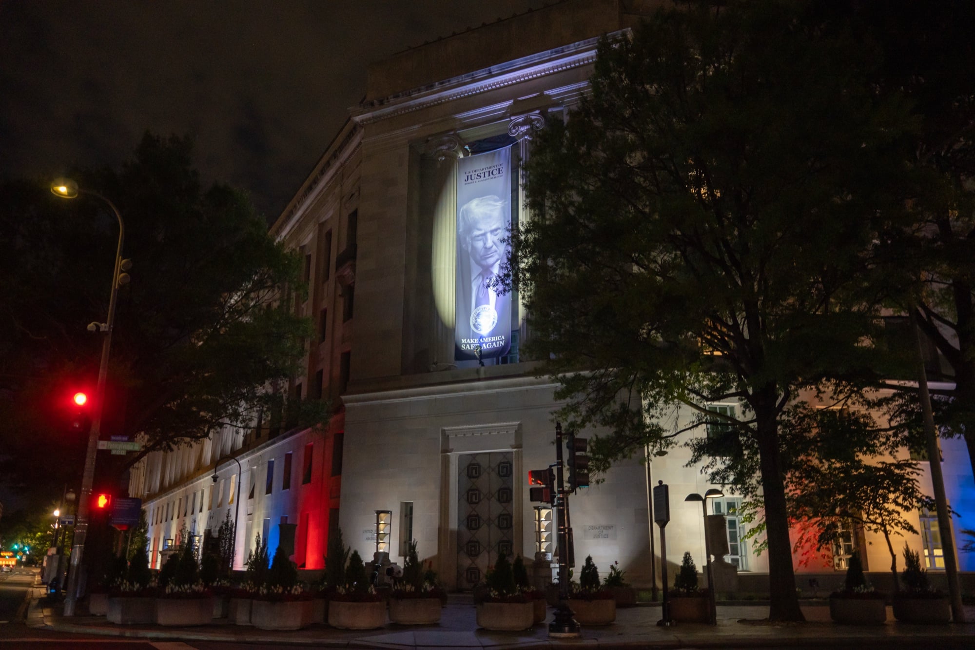 A banner of President Donald Trump hangs on the Justice Department headquarters at night.